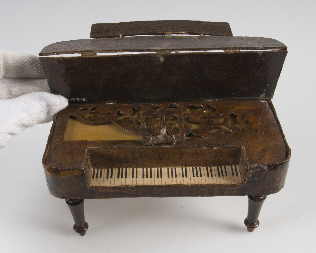 Leksak, taffel av mörkbrun och gulflammig ädelträimitation. Klaviatur av papper. På undersidan står med bläck: i Rde 20 öre. 