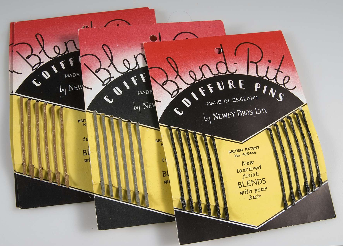 Pappask innehållande hårspännen uppsatta på originalpapper. Förpackningen är röd/vit/svart och innehåller 14 papper med 12 smala hårspännen i två olika färger på varje. På asken tryckt text: Blend Rite COIFFURE PINS. På varje papper tryckt 40 öre.