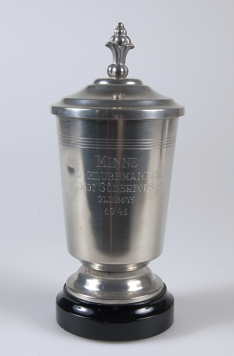 Idrottspris av metall i form av en pokal med lock på underlag av svartmålat trä. På pokalen inskriptionen: MINNE AV KLUBBMATCHEN MOT SÖDERFORS, ODLBOYS 1941.
