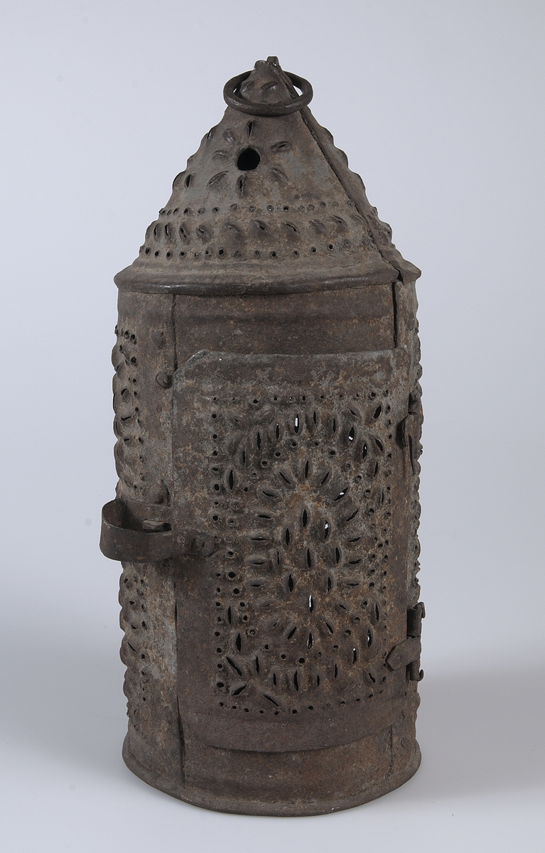 Cylindrisk lykta av järn med genombruten dekor och spår av blågrå färg. Öppningsbar lucka. Ring för upphängning i toppen.