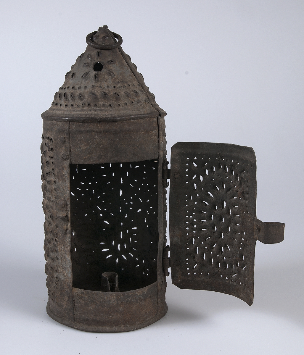 Cylindrisk lykta av järn med genombruten dekor och spår av blågrå färg. Öppningsbar lucka. Ring för upphängning i toppen.