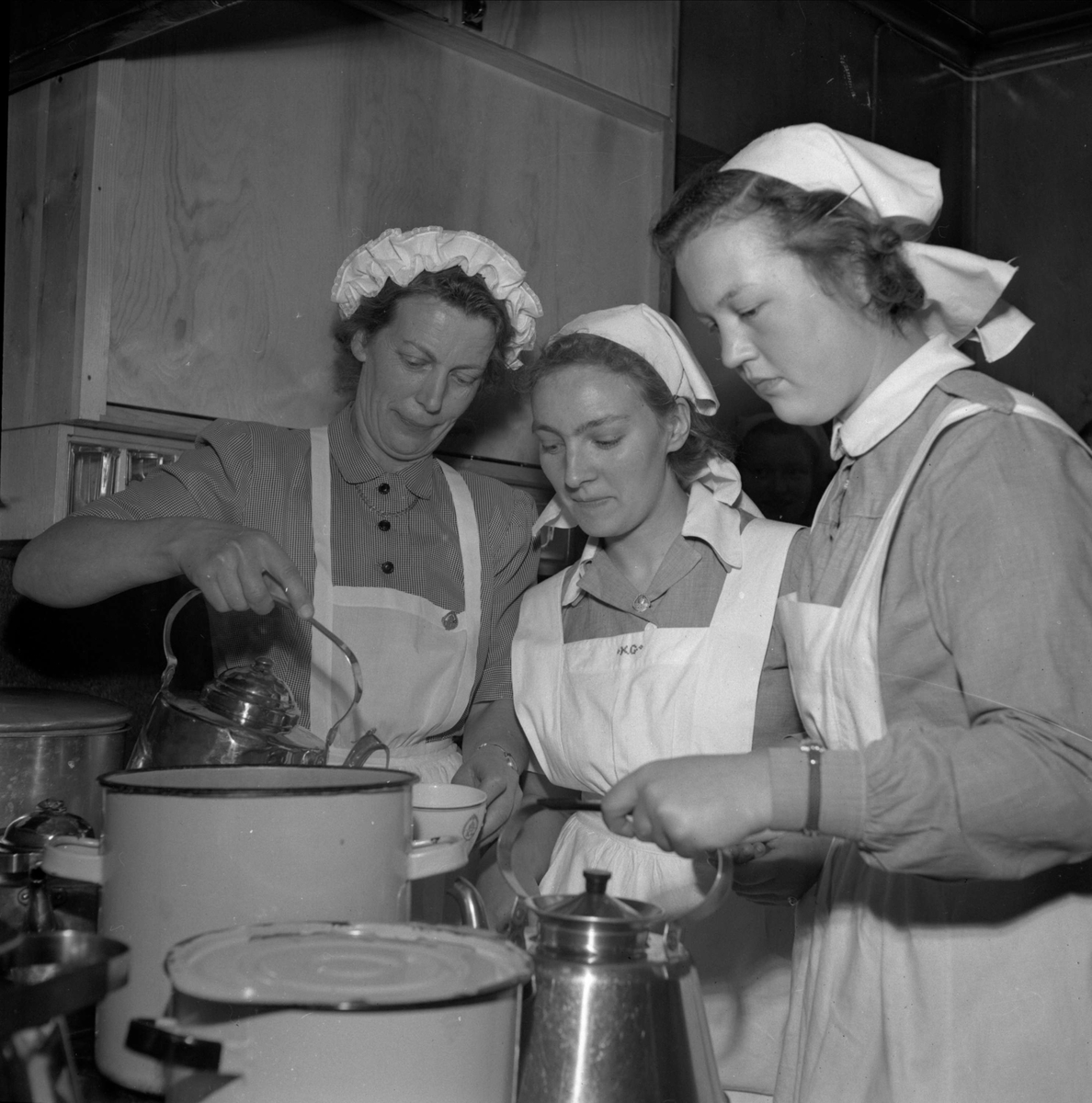 "Lanthushållslärarinnan Svea Carlson förbereder avskedskaffet tillsammans med eleverna Kerstin Gunnarsson och Anita Zettergren"