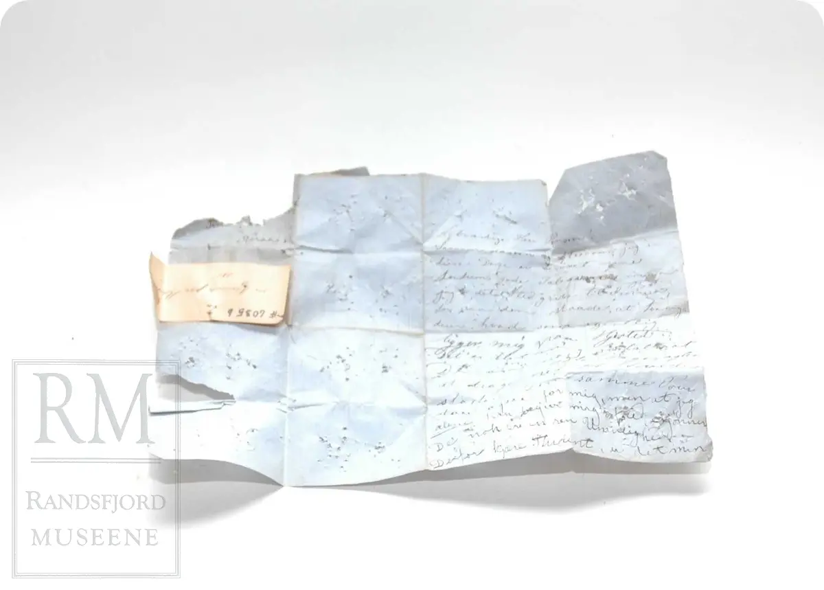 a: Liten dukke i stoff. Flatklemt. To underskjørt, skaut. b. Papir med håndskrift stilet til "Student Nielsen" og merket "Fra en Venninde paa Røros 1865" Tekst: Agtværdige Herr Person! Saasom, dasom og eftersom jeg i disse Dage er berøvet mine fordums gode Talegaver maa jeg i dets Sted gribe til Pennen, for paa den Maade, at faa sige Dem, hvad som egentlig ligger mig paa Hjerted. Det er blit mig fortalt, at De om nogle Dage, agtes at drage ned til Hovedstaden. Den samme Tour staar ogsaa for mig, men at jeg alene kan begive mig afsted skjønner De nok er en Umulighed. Derfor kjære Student, er det min inderlige Bøn til dem, om jeg kan faa slaa Følge med. Jeg ser dem an for at være en ret paalidelig og god Reisefælle, og vover jeg da at gjøre Dem dette Spørgsmaal. Haaber da at De unskylder min Nærhed, slutter jeg disse Linier. Det er mig meget om at gjøre at jeg allerede i Dag kunne faa et par Ord til Svar. Modtag den bedste Hilsen fra Deres hengivne og forbundne Simonette"