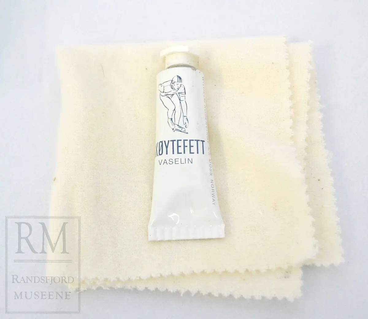 a-b) Skøyter: av svart skinn m / pløse og kant av beige skinn.Røret på skøytejernet avsluttet med plast i begge ender. 
c) plastpose til skøytene.
d) plaststykke.
e-f) Pappeske m/lokk. Brun papp med svart trykk på lokket.
g) pusseklut)
h) skøytefett i tube.