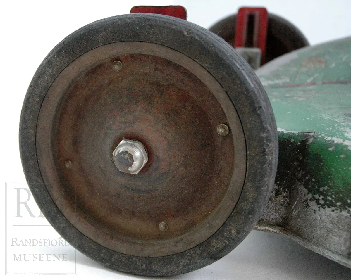 Gressklipper i aluminium med 4 gummihjul. Motor midt på. Motor har boks festet på siden. Metallhåndtak. Gresset blåses ut til høyre.