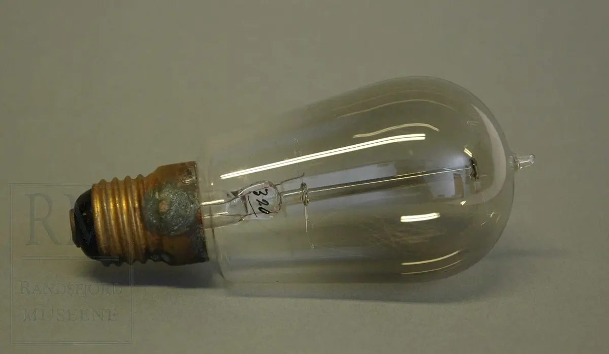 Til elektrisk belysning. Messingsokkel med gjenger. Glasset i kolben gjennomsiktig. Tupp i enden