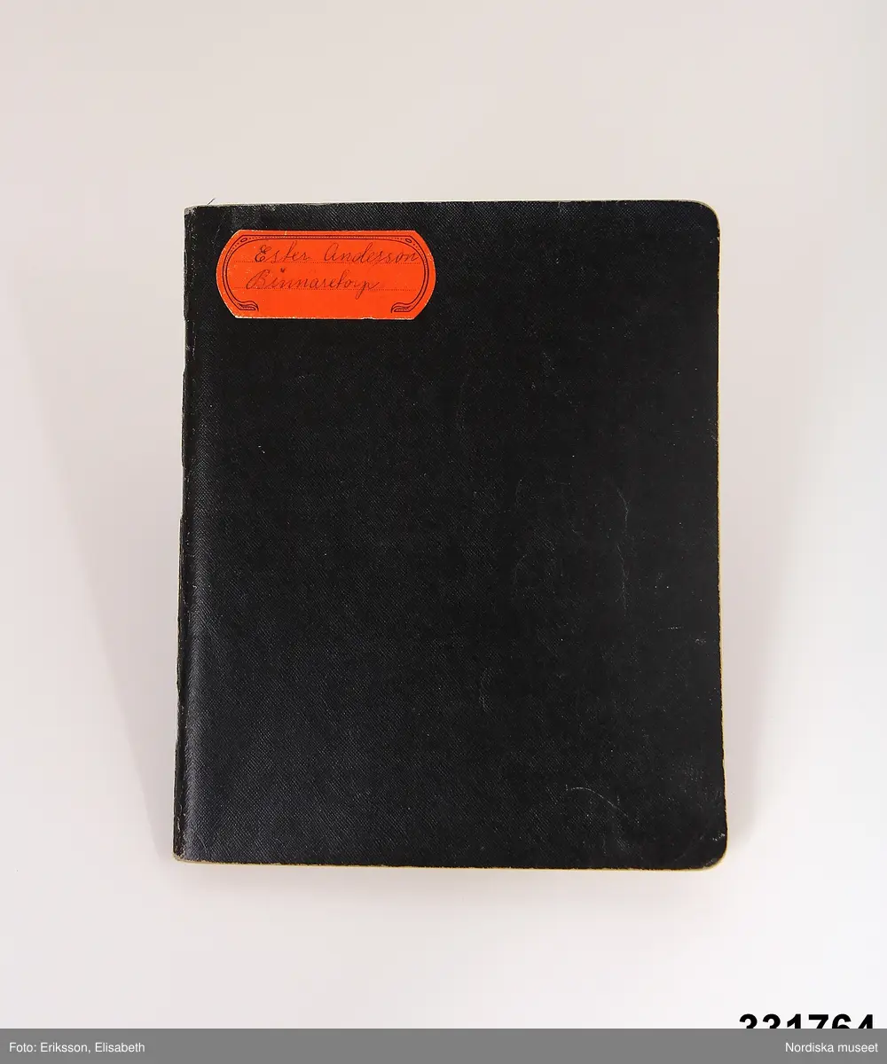 Vävbok, svarta vaxdukspärmar och inlaga med rutat papper.  I boken handskrivna anteckningar om vävning (vävbeskrivningar och vävnotor). Ex. på rubriker "Garnberäkning / Gardin Myggfjäll / Dräll 10 skaft / Handduk Gåsögon /  Halsduk Kypert / Gardin Droppdräll / Enkelt Munkabälte Möbeltyg". Orange etikett på framsidan "Ester Andersson / Binnaetorp". På insidan av främre pärmen tryckt "ESSELTE  3660/60 R." samt handskrivet Ester Andersson / Binnaretorp / Gullaboby"
/Anna-Karin Jobs Arnberg 2013-05-30