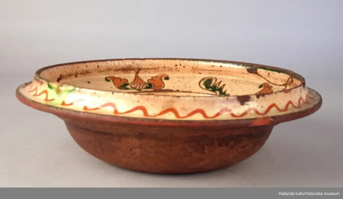 Fat av lergods, insidan täckt med vitlera med ristad dekor och grön glasyr. Märkt 1779.