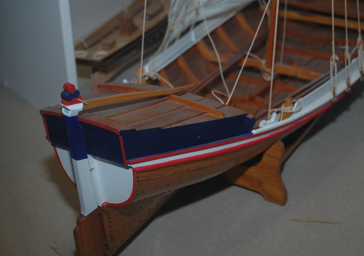Klinkbygget  modell med løfting og ror, rorkult, 4 årer (NSM.07948-51), mast, tiljer,2 tofter. Rigget med seil. Lakket skrog, øverste bordgang malt hvit med to smalere røde linjer på hver side. Løfting blå sider. Akterspeil hvitt. Ror over vannlinjen hvitt og blått.  Målestokk 1:18.