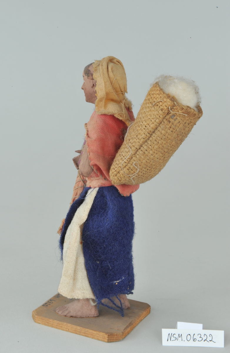 Viser kvinne med barn på armen og kurv på ryggen. Venstre arm mangler fra albuen og ned.