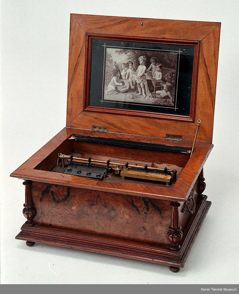 Med en plate: Die Morgenglocken. Nr. 3082. Bilde nr. 6 viser en tilsvarende spilleautomat i god stand. Den viser at det opprinnelig har vært et glasslokk over platen. På den registrerte gjenstanden er bare deler av den sorte rammen som glasset har vært festet i igjen.