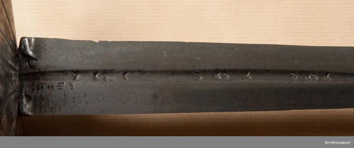 Klingan märkt med P-stämpel och "(CO)". Bredd vid fästet: 34 mm.

Fästet med upp-/nedvänd, äggformig knapp m icke ursprunglig låg nitknapp. Kavellindning av snodda mässingstrådar i reglementsenligt mönster är av senare datum. Randad, flat, svärtad parerplåt; något mindre på insidan än på utsidan. Dess kant är svagt runduddad och den undre sidan har en ornering i form av radialt ordnade ränder. "Nr: 191" inputsat. Handbygeln m förtjockning på mitten är intappad i knappen. Från parerplåten utgår en svängd, yttre sidobygel och ansluter till handbygelns övre del. Parerstången nästan rakt utstående m ett droppformigt avslut. Från parerplåtens insida utgår vertikal tumbygel. 

Klingan tveeggad m flat ås och hålslipning på bägge sidor. I dessa äro inslagna otydliga bokstäver "(CO)" och P-stämpel.