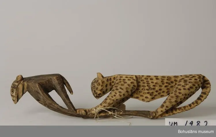 Föremålet visas i basutställningen Uddevalla genom tiderna, Bohusläns museum, Uddevalla.

Ur handskrivna katalogen 1957-1958:
Träskulptur; leopard och antilop?
L. 41 cm.
Leopardens fläckar brända in m. ngn. stpl; antilopen strimmig på huvudet, hornen saknas.
Trasig på flera ställen, lagad. Infödingsarbete, Sydafrika.

Lappkatalog: 9

Ernst William Nomell var ett av tio barn son till grosshandlarparet Johan August Nomell  och Elise, f. Kullgren i Uddevalla. 
Han arbetade som ingeniör vid diamantbolaget De Beer i Kimberley.