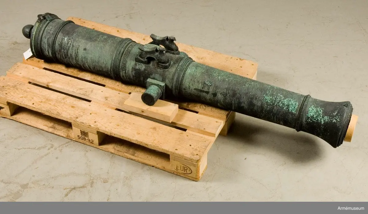 Med årtalet 1803 strax framom och inskriften: "St. Petersburg", å ryska, strax bakom delfinerna.

På den vänstra tappens fria ände: "No 98", på den högra tappens fria ände: 20 pu  27 fu  - "20 Pud 27 Funt". Fängpannan har formen av ett manshuvud utan skägg, och befinner sig på bottenplanet. /v. Tepfers.

Märkt på tappstycket med 1803.