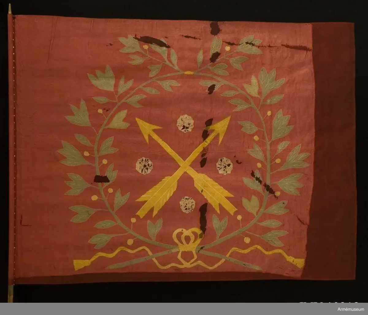 Fanduk av röd taft med insydda emblem: Närkes sköldemärke, två korslagda pilar i gult, med fyra i vinklarna ställda rosor i vitt (gulvitt), omgivet av en lagerkrans i grönt, bildad av två korslagda kvistar, nedtill hopknutna med gula band med tofsar. Skuggning och mönstring i plattsöm. Stång av vitmålad furu, senare än duken, nedtill försedd med doppsko, avbruten och försedd med två järnskenor.