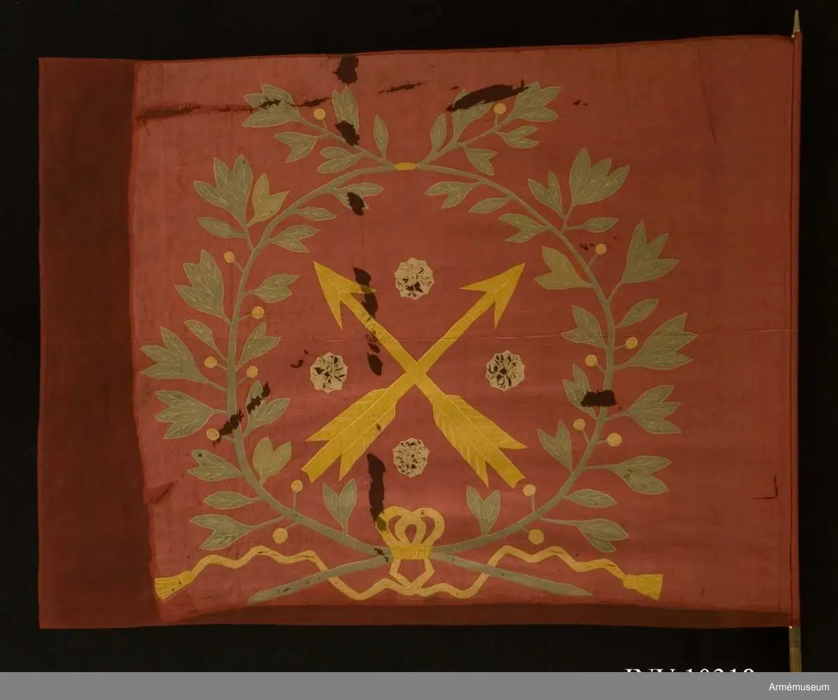 Fanduk av röd taft med insydda emblem: Närkes sköldemärke, två korslagda pilar i gult, med fyra i vinklarna ställda rosor i vitt (gulvitt), omgivet av en lagerkrans i grönt, bildad av två korslagda kvistar, nedtill hopknutna med gula band med tofsar. Skuggning och mönstring i plattsöm. Stång av vitmålad furu, senare än duken, nedtill försedd med doppsko, avbruten och försedd med två järnskenor.