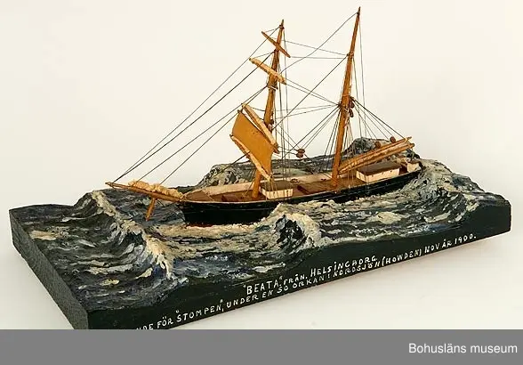 Bramsegelskonaren Beata från Helsingborg, 
Tillverkad av kapten John Emil Olsson (1880-1950), Fiskebäckskil på Skaftö i Lysekils kommun på 1940-talet.
Trä, metall, lintråd, tyg, gips.
Höjd 20 cm, längd 32 cm, B 9 cm. Platta längd 42 cm och bredd 20,5 cm. Okänd skala.
Vattenlinjemodell med två master, grönmålat skrov, röd bottenfärg, övriga detaljer vitmålade eller lackade. Stående och löpande rigg med utskurna block. Undre märssegel av snidat trä, revade segel av gasväv samt med däckshus, lastluckor och ratt. Monterad på utskuren platta med modellerad och målad gipssjö.
På plattans långsida har kapten Olsson textat med vita tryckbokstäver:
"BEATA". FRÅN HELSINGBORG 
LÄNSANDE FÖR "STOMPEN", UNDER EN SO ORKAN I NORDSJÖN (HOWDEN) NOV ÅR 1900.

Modellen föreställer hur fartyget förlorar däcklasten överbord i en orkan i Nordsjön.
I Sjöfartsbok för John Emil Olsson utfärdad vid Uddevalla Sjömanshus framgår att han var mönstrad som matros på Beata som gjorde fyra resor från Hasle på Bornholm till England via Norrland under befälhavare N. P Nilsson den 16 mars - 11 december 1901.

Definitioner:
Seglet på näst understa rån på råriggad mast kallas undermärssegel eller stump. 
Vid hårt väder beslogs fartygets alla segel utom undermärsen och man seglade "för bara stumpen". 
Blev vädret värre fick man försöka rida ut stormen och ligga bi för sviktade stumpar. Då revades halva stumpen så att bara en trekant blev kvar på rånockens ena sida.

John Emil Olsson var mönstrad på Beata  med hemmahamn Helsingborg som matros  16 mars t o m 11 december 1901 för resa  Hasle - England via Norrland (fyra resor) . 
Ur handskrivna katalogen 1957-1958:
"Beata"
Modell på platta. L. (från för till akter) 25. Föremålet helt.
Från kapten Olssons saml., Fiskebäckskil.

För ytterligare information om John Emil Olsson och förvärvet, se UM005807.

Föremålet presenterat på Bohusläns museums hemsida år 2009 - 2013, webbutställning "John Emil Olsson Fiskebäckskils sjöfartsmuseum".