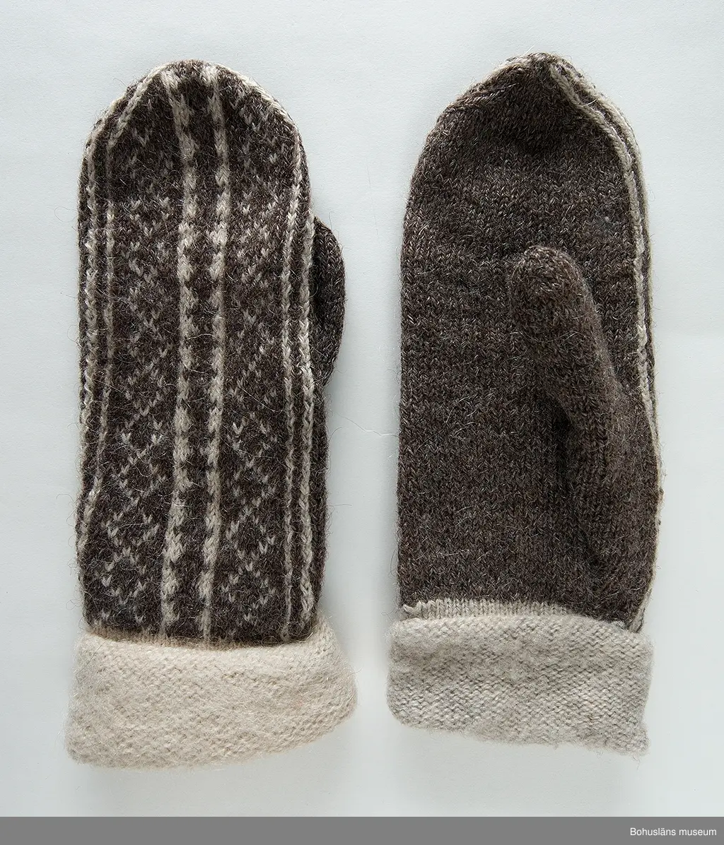 Stickade tumvantar i slätstickning med slätstickad mudd, med avigsidan utåt och mönstrat parti på ovansidan. Partiet är mönsterstickat i brunt och vitt mot en brun botten. Muddarna är stickade i naturfärgad ull som sedan blivit uppruggade med borste. Mönstret "Vävnaden" är komponerat av Emma Jacobsson. Litet slitna men välbevarade.