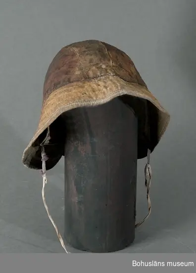 Huvudbonad vid bland annat fiske. Skyddar mot regn och vattenstänk.
Fodrad med rosafärgad bomullsflanell.
Isydd lapp anger storlek 60.

Ingår i redskapsbestånd ur sjöbod från Hällsö, Havstenssund, Tanum sn.
Se UM017521