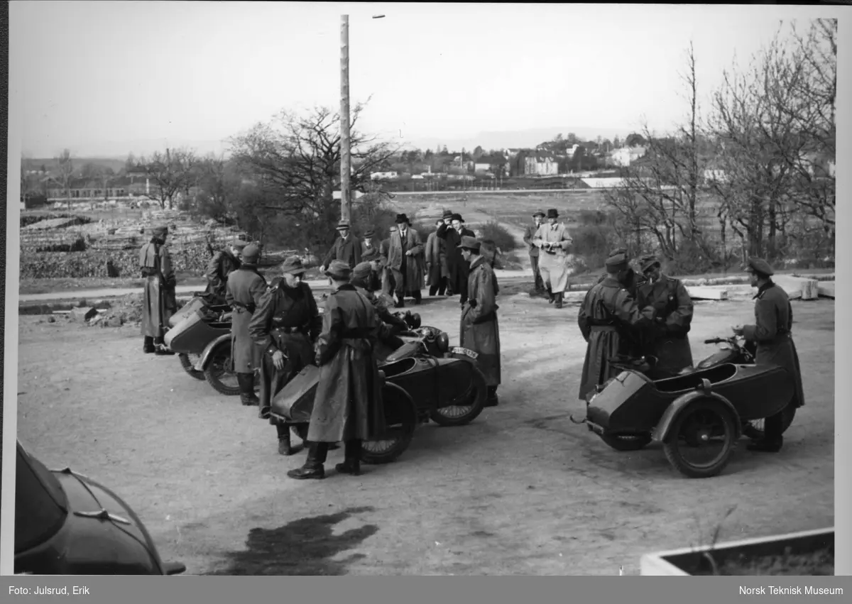 Foran Kringkastinghuset 8 mai 1945 kl 0700; tyskerene drar (motorsykler med sidevogn) og nordmennene kommer (til fots), fra venstre O Midttun, Th Diesen og Knut Tvedt