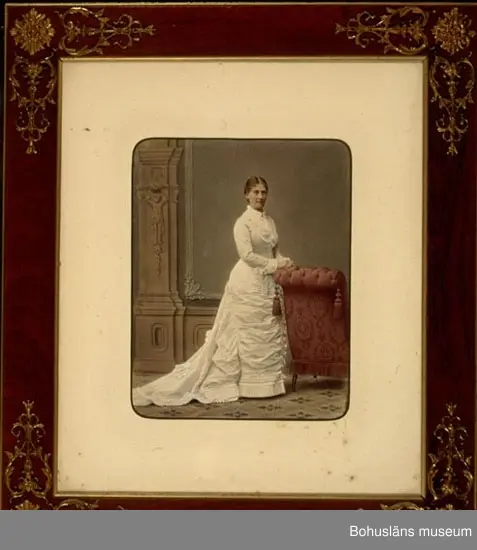 Handkolorerat fotografi av Pauline Ekelund, född Berg, 1843-1881, i brudklänning (nu förvarad i Bohusläns museum, se UM59.10.001). Monterat i mahognyram med mässingsornament, glasat.
På baksidans tunna bruna skyddspapper, som mestadels har fallit av på grund av skörhet, finns en linsformad stämpel med tryckt text: E. OHLSEN'S GULDLISTFABRIK Göteborg.

Pauline Ekelund gift med sedemera överstelöjtnanten Frithiof Ekelund född 1838 död 1915. Bröllopet stod 7 oktober 1879 i Rådhussalen Uddevalla. Inbjudningskort se Bohusläns museums arkiv Avd. Enskilda arkiv Barks arkiv samt som kopia till UM59.10.001 i bilagepärm. 
Makarna Ekelund ligger begravda på Norra kyrkogården, Uddevalla. 
Brukaren och givaren systrar döttrar till konsul Alban Thorburn och med släktband till Ekelunds via Bark.