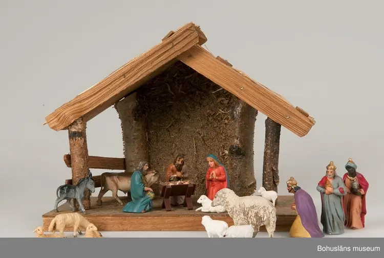 Stall med halmtak, trästolpar samt golv och vägg av masonite. Märkt UM19818:1
18 st figurer tillhör julkrubban. De är märkta UM19818:2.
Krubba, Jesusbarnet, Maria, Josef, en herde, de tre vise männen, en åsna, en oxe, tre liggande får, fem stående får varav ett betydligt större.
En av de tre vise männen märkt: Germany
Elastolin brukar denna typ av plastisk massa benämnas - egentligen ett  tyskt inregistrerat varumärke på en kompositmassa.