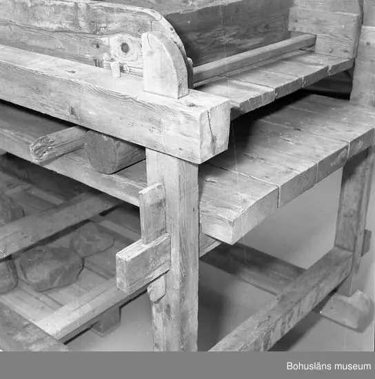 Trämangel med vagga för stenen. Två tjockare, två tunnare.
Beata Olsson  öppnade första lanthandeln i området vid Brattås, Morlanda (Henån) på 1880-talet i hus vid vägen. Mangeln uthyrdes samtidigt som lanthandeln drevs. Den var placerad i ett magasin bredvid och hyrdes av byns (Brattås) invånare. Under senare år användes den mest av
Beata Olssons släktingar. Nedmonterades något år innan den skänktes till museet.
Beata Olsson kom från Tegneby  socken. Givaren lanthandlare i Brattås.
Nuvarande affären flyttad snett över vägen längre ned i backen.