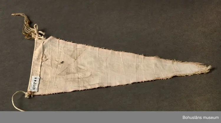 Trekantig vimpel. Naturfärgad bomull med textiltryck. Röd kant och i grönt bild av Strömstads kyrka och namnet "Strömstad".
Sammanhör med UM026180 - UM026184.
Användar- och förvärvsuppgifter se UM026180