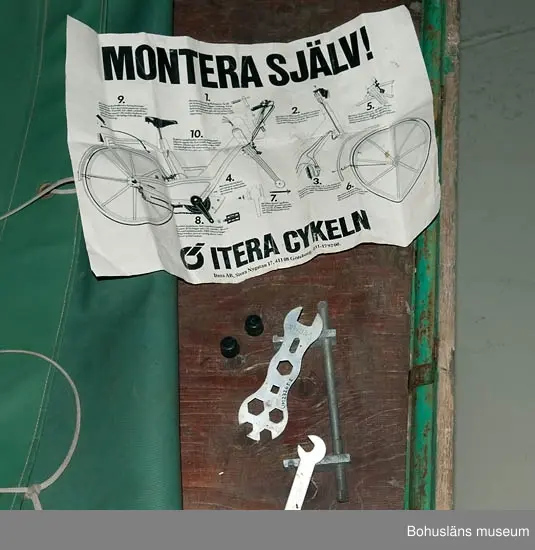 Måttuppgifter flaket: 195 x 195 cm; höjdmåttet avser höjd vid styret.
Grön presenning, fästad i flakets bakre del.
Mopeden är inköpt i Strömstad 1973 och använd på Sydkoster till slutet av 200
Mopeden ingår i insamlingen i projektet Moderna skärgårdsbor, UM027511 - UM027595 och kommer från Sydkoster.