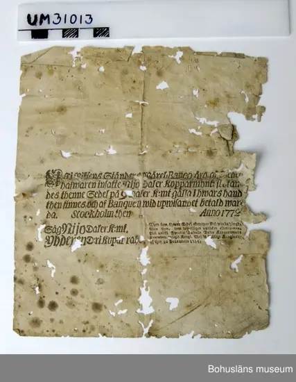 Föremålet visas i basutställningen Uddevalla genom tiderna, Bohusläns museum, Uddevalla.

Pappersedel, s. k. transportrsedel av linnepapper. 

Överst skrivet för hand ett oläsligt nummer, (057?)
Två stora runda vitstämplar med präglad text:
Till vänster: Omskrift på latin (bl. a. ET SECURITAS) med en strålande sol och de tre första riksståndens emblem i rokokostil, till höger: SVERIGES RIKES STÄNDERS BANCO TRANSPORT-SEDEL. Därovanför riksvapnets tre kronor.

Mitt på sedeln tryckt text i frakturstil  i svart:

Uti Riksens Ständers Wäxel=banco äro af Sedel=
hafwaren insatte Rijksdaler Kopparmynt: skolan=
des thenne Sedel på 9 Daler k:mt gälla i hwars hand
then finnes, och af Banquen wid uppwisandet betald war=
da.       Stockholm then (oläsligt handskrivet) datum)  Anno 1772
Såg Nijo Daler k:mt.
Yhderen D:rekuparraha (finska)

Then som thenne Sedel efterapar skal warda hängd;
Men then, som bewisligen upptäcker efteraparen,
skal undfå Fyratio Tusende Daler Kopparmynts
Praemium, enligt Kongl. Maj:ts Nådige Kunggörelse
af then 20 Decembris 1754.

Två svårläsliga namnteckningar.

Spegelvänt baksidestryck i svart.

Kraftiga angrepp av boklöss., vikskador, trasiga kanter, fläckar, tejpbitar. 

Okända förvärvsomständigheter.

Ur Nationalencyklopedin, NE.se: Transportsedel
Riksens Ständers Bank, grundad 1668 - Sveriges riksbank - införde 1701 en transportsedel, dvs. man inbetalade en summa och fick ett kvitto som gällde som sedel och kunde användas som betalningsmedel. Genom påskrift "transporterades" sedeln på annan person. Från 1745 utgav banken sedlar av lägre valör utan inlösningsrätt i silver. Följden blev ett slags pappersvaluta.

Ur Kungliga Myntkabinettets hemsida:
Riksens ständers bank började 1701 ge ut transportsedlar, det vill säga sedlar utställda på namngiven innehavare men med rätt för denne att genom anteckning överföra (transportera) sedeln till någon annan person.