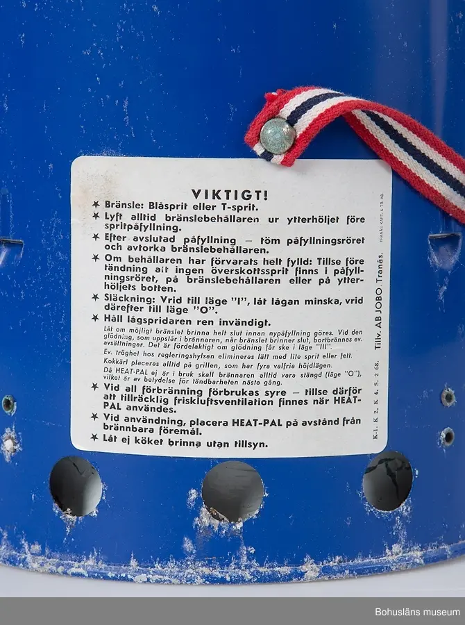 Rund kamin, värmare  av märket "BOAT HEAT-PAL".Underdel av blålackerad metall med brännre för blåsprit eller T-sprit. Överdel med genombruten skyddskåpa.
Genom att lyfta av överdelen kan värmaren även användas som ett litet kök för ett kärl på gallret.
Bärrem av kraftigt vävt band i rött-vitt och blått.
Fastkklistrade etiektter med instruktioner och säkerhetsföreskrifter
Korroderad.