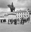 En grupp kvinnor och män samlade kring dubbelstatyn från 1915 på Kungstorget i Uddevalla