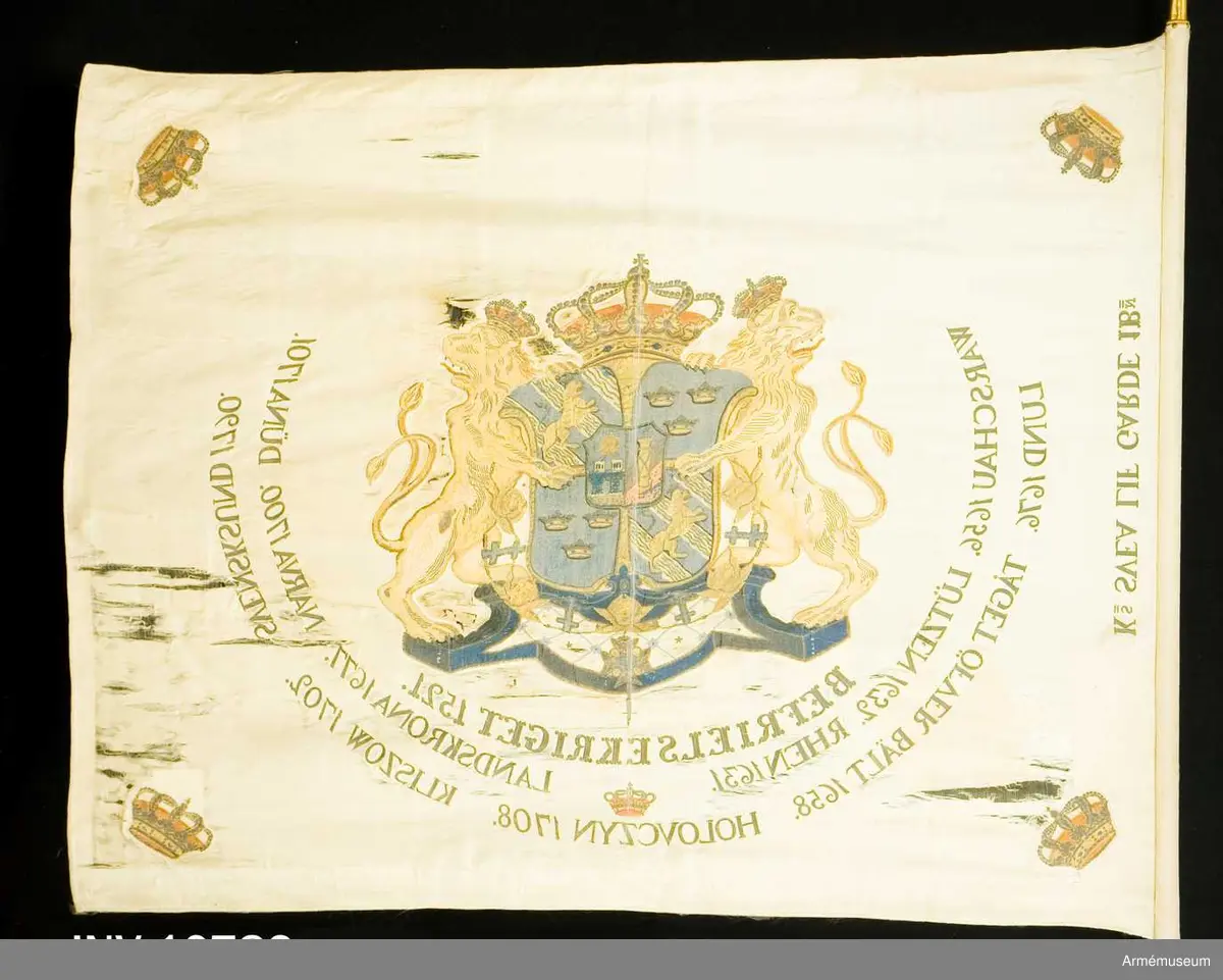 Duk av vit sidenkypert varå broderat lika å båda sidor, riksvapnet omgivet av segernamnen, slutna kronor i hörnen. Kravatt med guldfrans tillhör. Fanstången är vitmålad. Spets med Oskar II:s namnchiffer.