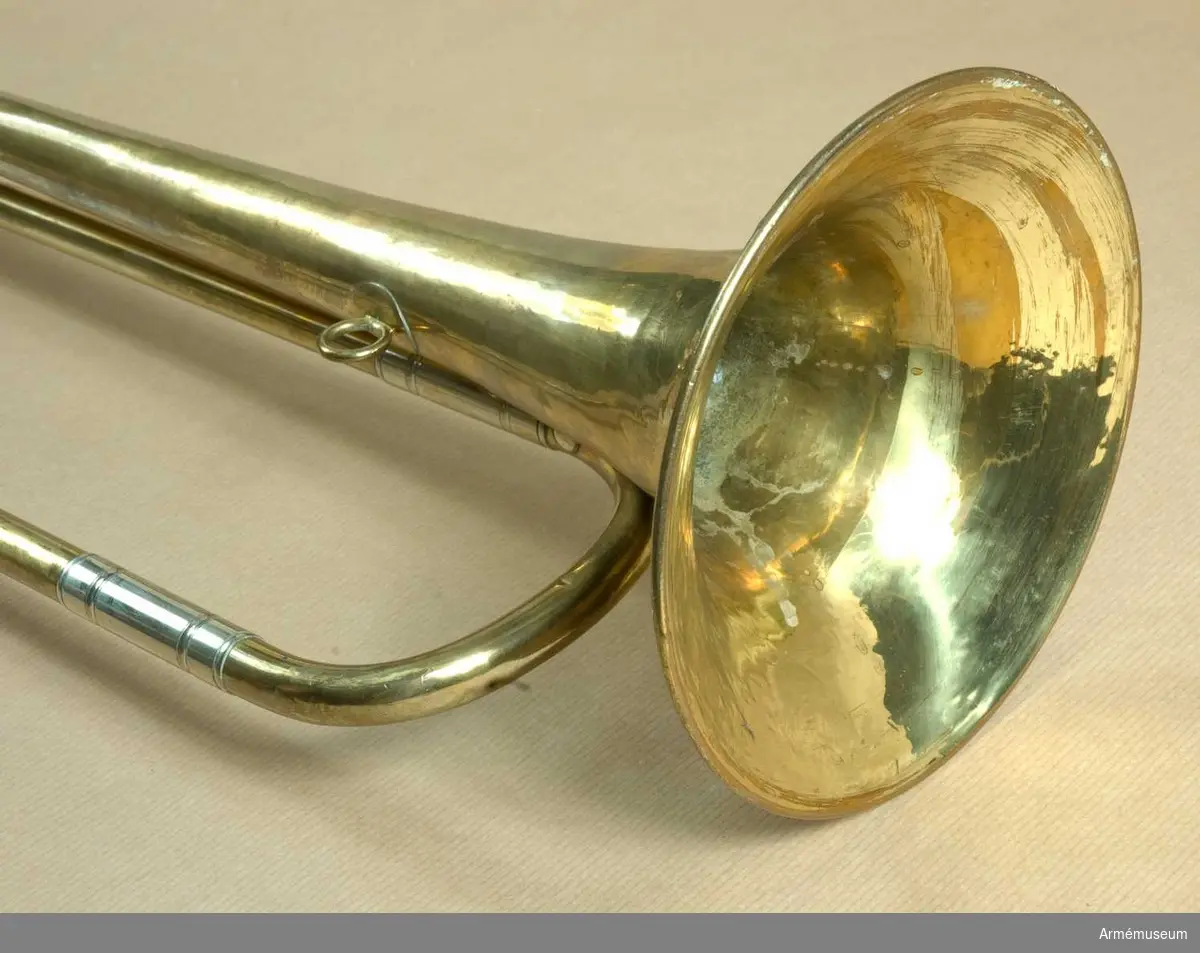 Trumpet av mässing och vitmetall med en vindling. Höjd utan munstycke 69 cm, med d:o 72 cm, diameter 15 cm. Trumpeten är signerad på klockstycket: Bohland & Fuchs, Graslitz. Texten är dock nästan bortputsad.