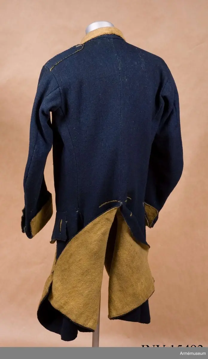 Rock av blått kläde med gul krage och ärmuppslag. Fodrad med gul boj i livet och med linne i ärmarna. Försedd med tennknappar.