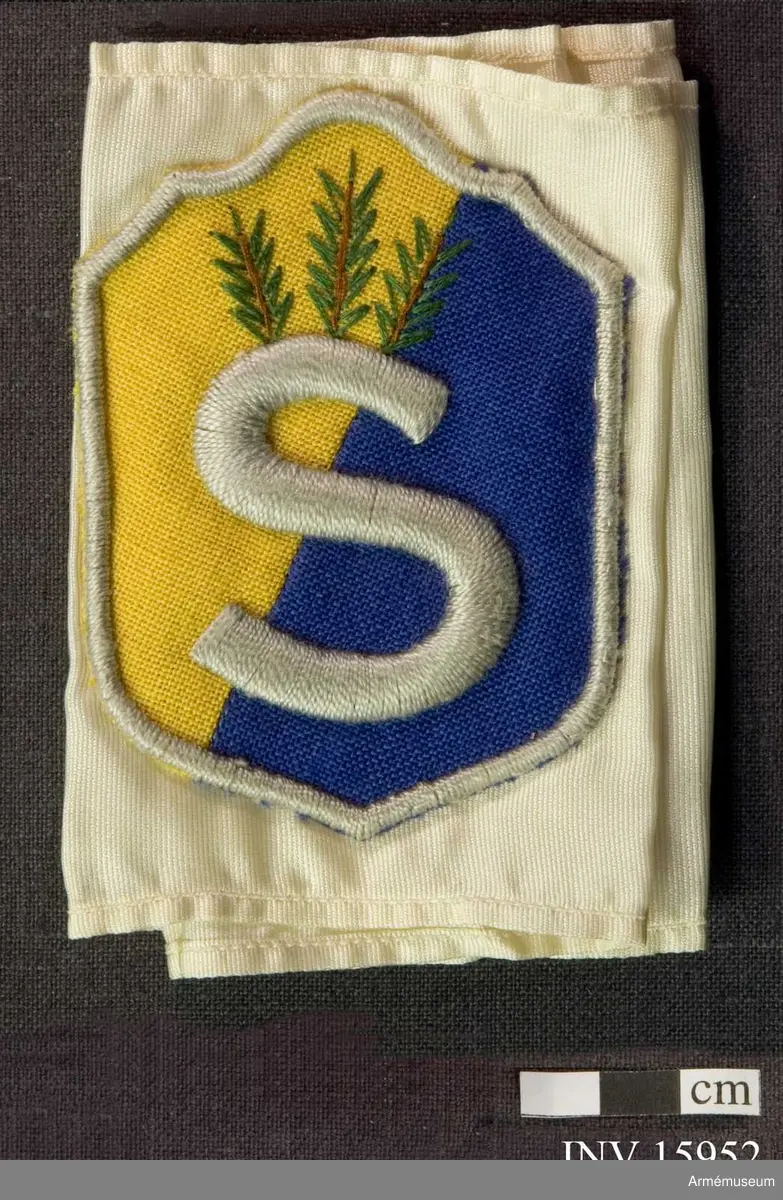 Grupp C I.
Armbindel - 10 cm bred av vitt sidentyg med påsytt  skyddskårsemblem broderad av silke, som består av två delar (blått och gult). Omkring emblemets kant och i mitten bokstaven  "S" (första bokstav i ordet skyddskår - suoluskunta på finska), broderad av ljusgrått silke. Ovanför bokstaven "S" tre små grankvistar broderad av brunt och grönt silke.