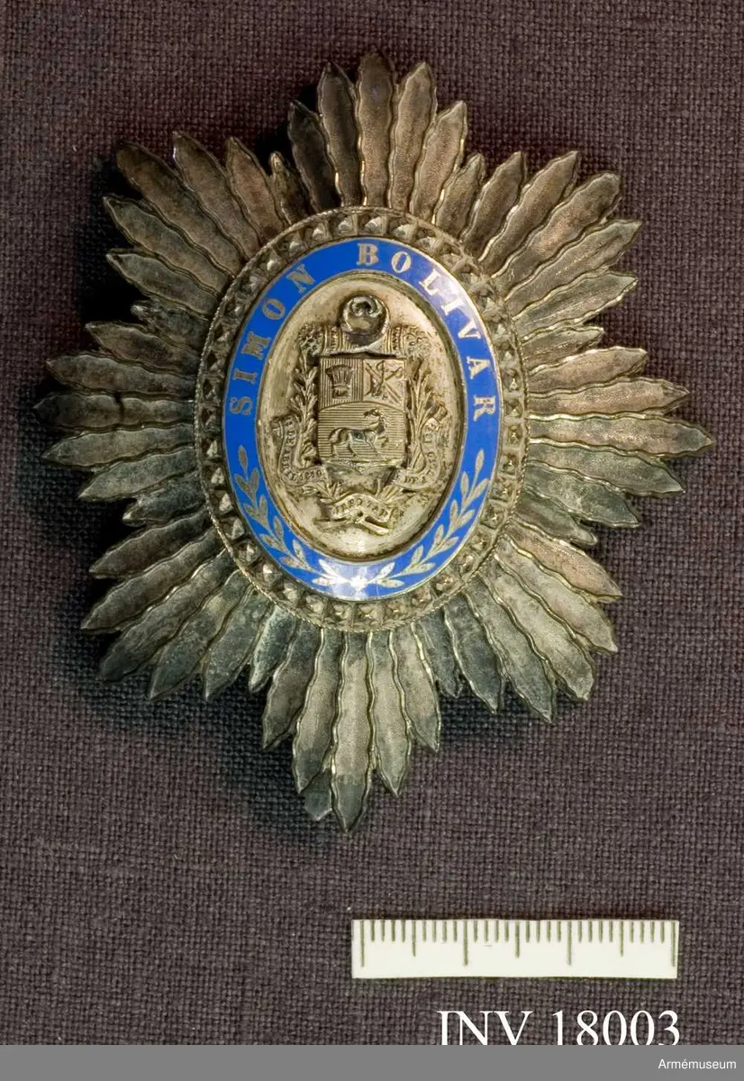 En oval silversol av åtta stålknippen, vart och ett bestående av fem olika långa strålar, symmetriskt ordnade. Den ovala mittskölden utgöres ytterst av en rand stora, facetteraden silverpärlor, därnäst en ram i blå emalj, å vilken i silverbokstäver läses: SIMON BOLIVAR, nedtill två från varandra vända kvistar. 

Mittpartiet är av silver och upptages av en sköld innehållande Venezuelas vapen, en sädeskärve, två sablar, två fanor samt därunder, i räfflat fält en häst med bakåtvänt huvud. Ovanpå skölden två korslagda ymnighetshorn, på sidorna en lager- och en olivkvist, samt under skölden ett omkring kvistarna virat band, varpå läses 15 DE ABRIL 1810 LIBERTAD 5 DE IULIO 1813. 

På baksidan FAYOLLE POUTEAU Seur 180 G DE VALOIS, Fr DU SENAT & DE LA DEPUTES PALAIS ROYAL. /Beskrivning: Carl Peyron.