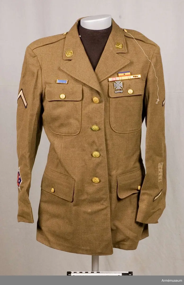 Vapenrock för amerikanska infanteriet. En class A uniform. Vapenrocken är från andra världskriget. Den är  enkelknäppt med 4 metallknappar och har  4 st utanpåfickor med lock. Framsidans insida är fodrad med bomullsväv. Axelklaffarna har inga emblem. På kragspegeln finns en  knapp märkt US. Vänster ärms övre del har ett märke med 4 st stjärnor och ett emblem (ett upp-och nedvänt V) som anger korprals grad. Längre ner finns 5 broderade band som anger " overseas service" och underst ett snedställt streck för 3 års tjänstgöring. Höger ärm har överst ett emblem för koprals grad, och längre ner ett märke: på blå botten med stjärnor och texten Guadalcanal.  Släpspännen: Unit citation with star 31 dec 43 Issued laped button - No time lost under AWL American Defence Service Medal, Asiatic Pacific Theatre Campaign Ribbon with two Service stars. Vapenrocken har tillhört Per Rabe under hans tjänstgöring i amerikanska armén under andra världskriget.