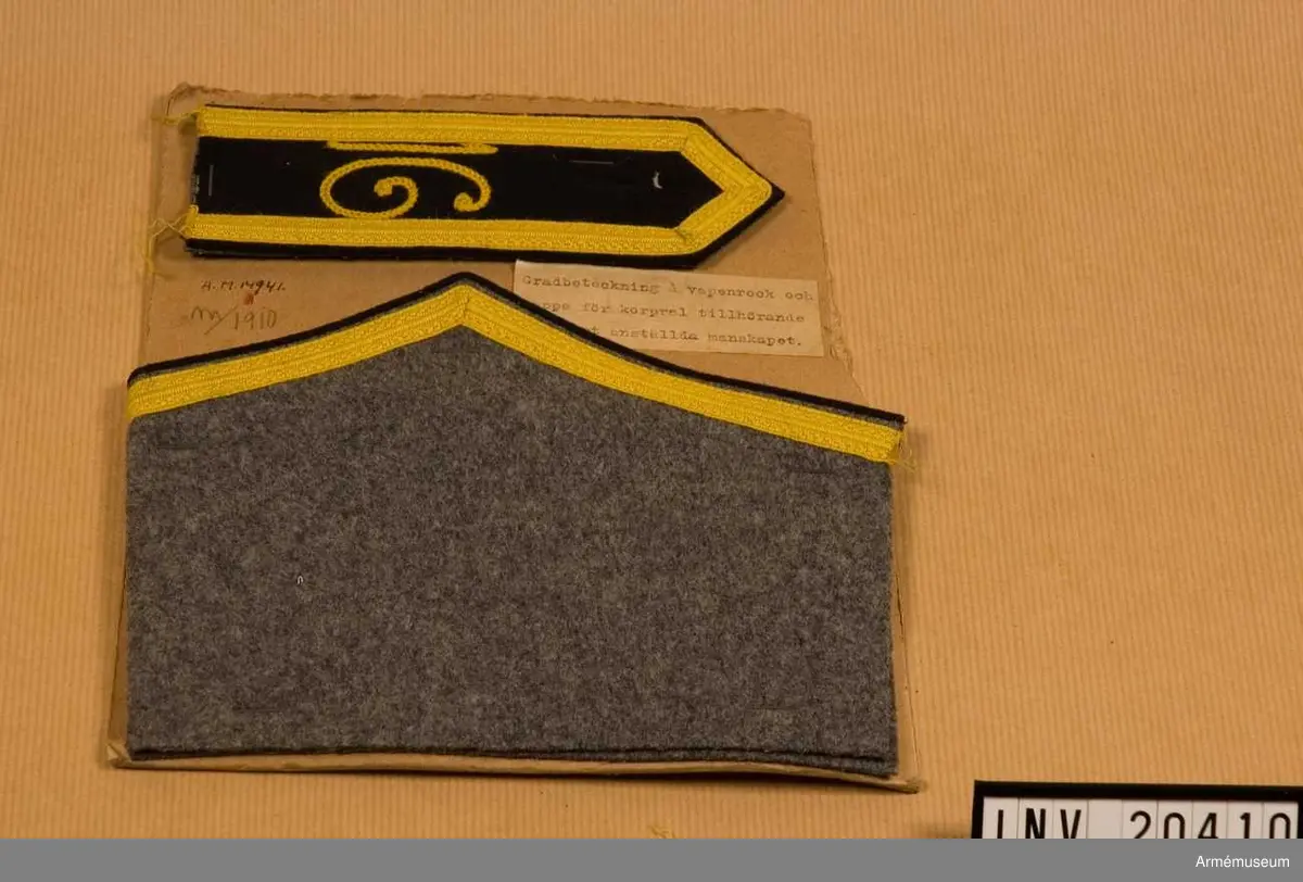 Grupp C I.
Med gradbeteckning för korpral tillhörande fast anställt manskap. För vapenrock och kappa.