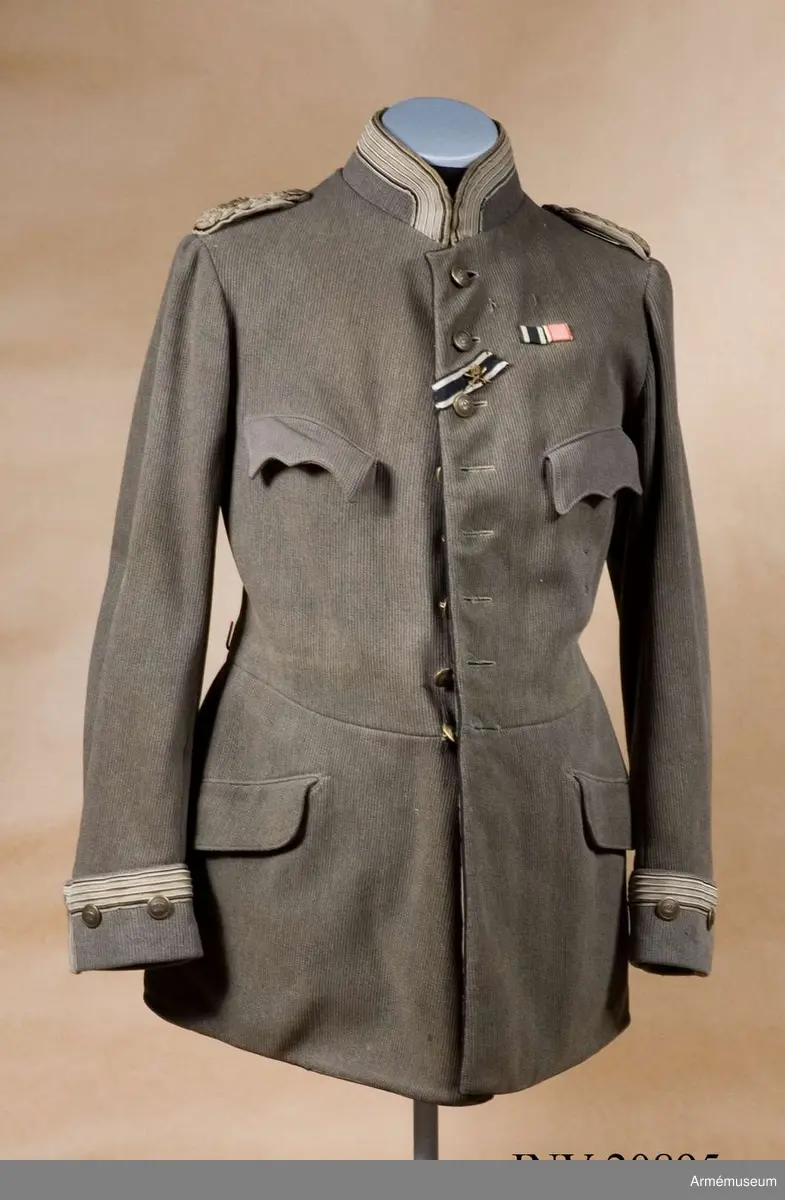 Av fältgrått diagonaltyg. Åtsittande med midjesöm. Enradig och har åtta knappar. På bakfickorna ett tvåuddigt lock med tre knappar. Baktill vid midjan sitter 2 hakar av mässing. Vid knäppningen på bröstet finns ett band till järnkorset (svart-vit-röd) med ett märke av metall. På detta märke finns två korslagda svärd och en krona. Högre upp sitter två ordensband, det ena är järnkorset. Axelklaffar med flätade tränsar av bomull med svart tyg under  tränsarna och under detta vitt tyg (svart och vitt var  I:a Kyrassiärreg:s färger). Axelklaffarna saknar stjärnor och tränsarna utvisar majors grad, stabsofficerstränsar. Högra axelklaffen har namnchiffer av metall: "F.W.R." (Fredricus Wilhelms Rex), den V saknar namnchiffer. Båda är fastsydda vid vapenrocken och har små knappar. Fickor. På bröstet två innerfickor med treuddiga lock och två större sneda med runda lock under midjan. Foder av brunt bomullstyg med två innerfickor (på bröstet och  på vapenrockens nedre del). Fickan på nedre delen är till för första förband. Knappar matt guldfärgade, d: 20 mm, med krona. De på axelklaffarna är av samma typ men mindre. Krage av samma tyg som vapenrocken, upprättstående med runda vinklar. På kragens övre kant finns ljusgrå galon av bomullssilke, b: 30 mm, med två svarta sidenband, b: 3 mm. Kragen har tre hyskor hakar och är fodrad med grönt tyg. Passpoaler av svart sammet längs rockens främre kant och på de bakre fickornas lock. Ärmuppslag, rakskurna av samma tyg som vapenrocken, 8 cm höga med galon av ljusgrått silke (kastade med två svarta sidenband 0,5 cm breda) omkring ärmuppslagen. Under galonen finns två  knappar.
Spänne med miniatyrordensband. Ordensband för Hohenzollernska husorden.