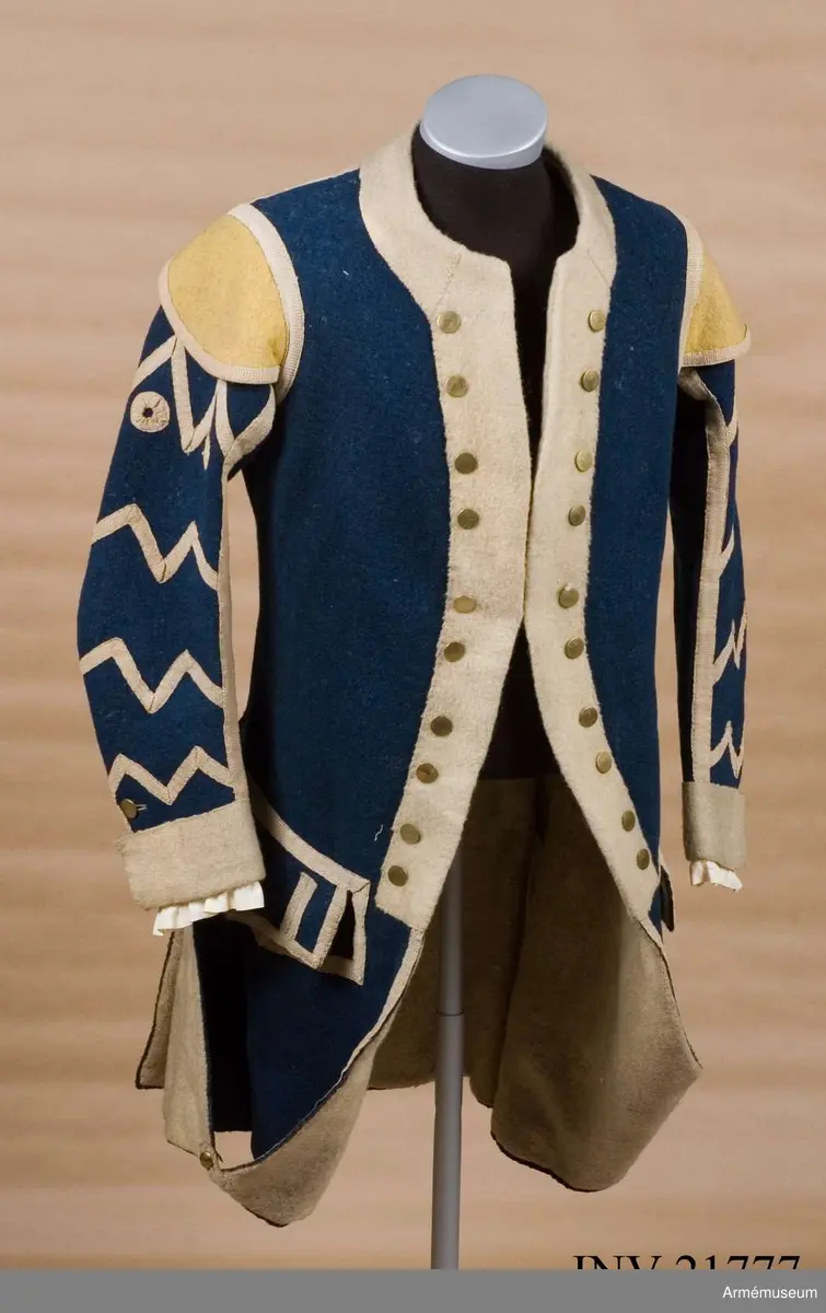 Rock av blått kläde med vita ärmuppslag och bröstrevärer av vitt kläde, gula axelkarmar, dekorationer av vävda vita band i tre olika bredder och släta mässingsknappar. Rocken är lång, med svängd mitt-fram-linje. Troligen nådde den nästan till knät på den som bar den. Den har 20 parvis ställda knappar fram, men knäpps kant i kant med två hyskor och hakar.
Den är konstruerad med hela framstycken som går runt till baksidan och bildar sidstycken. Delat bakstycke med mitt-bak-söm, samt tvåsömsärm. Sidsömmarna, ärmsömmarna och mitt-bak-sömmen är dekorerade med band. Två lågt ställda horisontella fickor fram med bandprydda ficklock, falska knapphål och två knappar vardera.
Skört med uppvik nertill fram. Sicksackdekorationer och rundlar på ärmarna.
Foder av vit boj i bålen, men oblekt bomull i ärmarna.