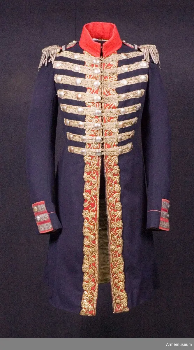 Blå knälång rock med röd krage och snörmakerier av förgylld metalltråd.
Renoverad och försedd med nya ärmuppslag omkring 1831.

Rocken är sydd av fint mörkblått kläde och har snörmakerier av guldlan fastsydda på en remsa av rött kläde på båda sidor om knäppningen mitt fram, samt i slitsen bak. Dessutom revärer över bröstet utförda av förgyllda tvinnade metallsnoddar, och 5 rader med 8 rent dekorativa knappar i varje rad. Knapparna är släta och svagt välvda, och av en försilvrad kopparlegering. Den egentliga knäppningen är 2 x 7 hyskor och hakar kant i kant mitt fram, samt 2 x 2 dito i kragen.
Rocken är konstruerad med fram- och sidstycken i ett, samt helt bakstycke utan söm mitt bak. Den har midjesöm med separat skört. Skörtet har fram- och sidstycken i ett, och två smalare bakstycken vid slitsen bak. Röd ståndkrage av fint kläde, fodrad med det samma.
Ärmarna är formade tvåsömsärmar med fasta ärmuppslag med smal röd passpoal och röd matta med tre "knapphål" av metallgalon som pryds av tre mindre knappar.
De svängda sidsömmarna bak är dekorerade med samma förgyllda tvinnade metallsnoddar som revärerna. Vid ryggslutet sitter två knappar.
Bålen är fodrad med gråvitt fint ylletyg, medan ärmarna är fodrade med oblekt eller vitt linne.

Till rocken hör ett par epåletter av silvergalon med fransar av krusade och vridna silvertrådar.