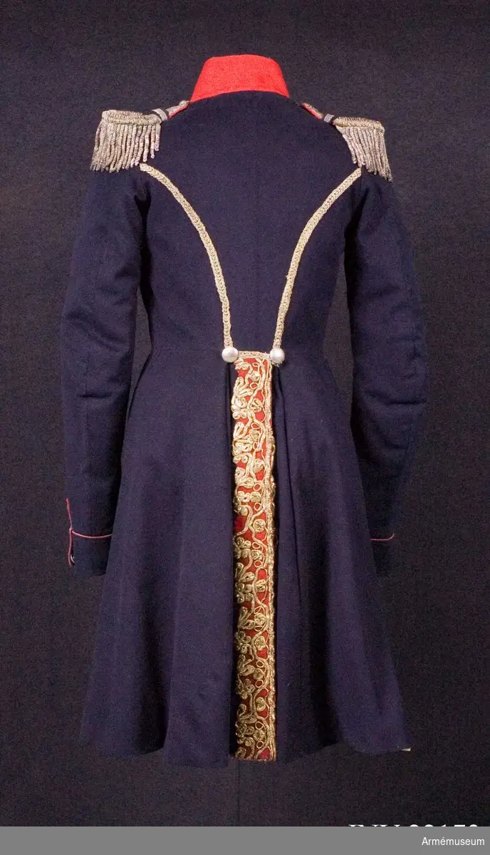 Blå knälång rock med röd krage och snörmakerier av förgylld metalltråd.
Renoverad och försedd med nya ärmuppslag omkring 1831.

Rocken är sydd av fint mörkblått kläde och har snörmakerier av guldlan fastsydda på en remsa av rött kläde på båda sidor om knäppningen mitt fram, samt i slitsen bak. Dessutom revärer över bröstet utförda av förgyllda tvinnade metallsnoddar, och 5 rader med 8 rent dekorativa knappar i varje rad. Knapparna är släta och svagt välvda, och av en försilvrad kopparlegering. Den egentliga knäppningen är 2 x 7 hyskor och hakar kant i kant mitt fram, samt 2 x 2 dito i kragen.
Rocken är konstruerad med fram- och sidstycken i ett, samt helt bakstycke utan söm mitt bak. Den har midjesöm med separat skört. Skörtet har fram- och sidstycken i ett, och två smalare bakstycken vid slitsen bak. Röd ståndkrage av fint kläde, fodrad med det samma.
Ärmarna är formade tvåsömsärmar med fasta ärmuppslag med smal röd passpoal och röd matta med tre "knapphål" av metallgalon som pryds av tre mindre knappar.
De svängda sidsömmarna bak är dekorerade med samma förgyllda tvinnade metallsnoddar som revärerna. Vid ryggslutet sitter två knappar.
Bålen är fodrad med gråvitt fint ylletyg, medan ärmarna är fodrade med oblekt eller vitt linne.

Till rocken hör ett par epåletter av silvergalon med fransar av krusade och vridna silvertrådar.