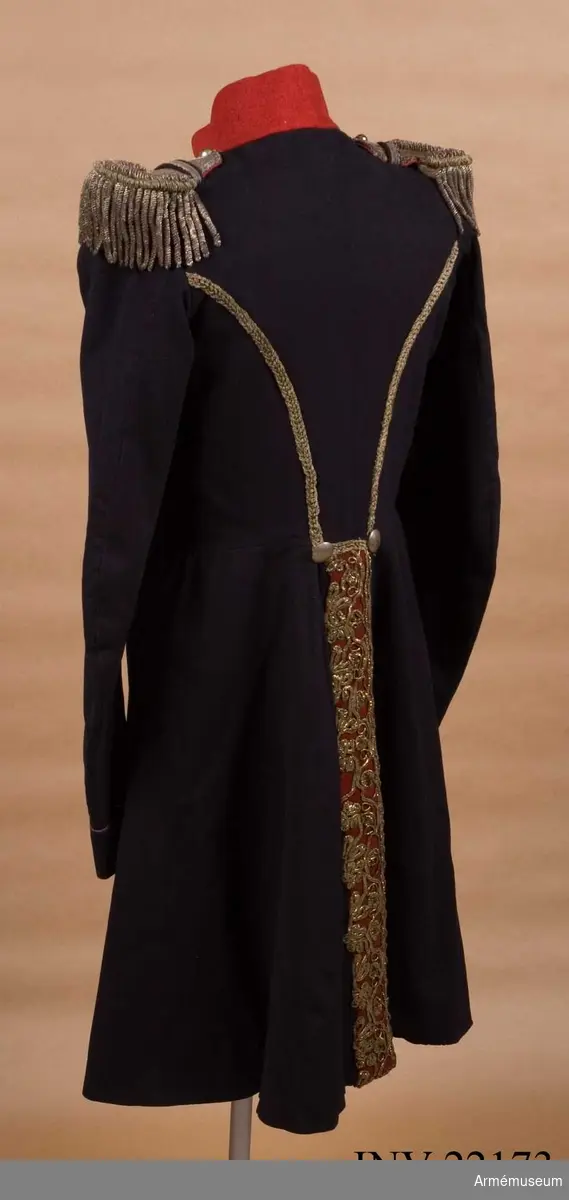 Blå knälång rock med röd krage och snörmakerier av förgylld metalltråd.
Renoverad och försedd med nya ärmuppslag omkring 1831.

Rocken är sydd av fint mörkblått kläde och har snörmakerier av guldlan fastsydda på en remsa av rött kläde på båda sidor om knäppningen mitt fram, samt i slitsen bak. Dessutom revärer över bröstet utförda av förgyllda tvinnade metallsnoddar, och 5 rader med 8 rent dekorativa knappar i varje rad. Knapparna är släta och svagt välvda, och av en försilvrad kopparlegering. Den egentliga knäppningen är 2 x 7 hyskor och hakar kant i kant mitt fram, samt 2 x 2 dito i kragen.
Rocken är konstruerad med fram- och sidstycken i ett, samt helt bakstycke utan söm mitt bak. Den har midjesöm med separat skört. Skörtet har fram- och sidstycken i ett, och två smalare bakstycken vid slitsen bak. Röd ståndkrage av fint kläde, fodrad med det samma.
Ärmarna är formade tvåsömsärmar med fasta ärmuppslag med smal röd passpoal och röd matta med tre "knapphål" av metallgalon som pryds av tre mindre knappar.
De svängda sidsömmarna bak är dekorerade med samma förgyllda tvinnade metallsnoddar som revärerna. Vid ryggslutet sitter två knappar.
Bålen är fodrad med gråvitt fint ylletyg, medan ärmarna är fodrade med oblekt eller vitt linne.

Till rocken hör ett par epåletter av silvergalon med fransar av krusade och vridna silvertrådar.