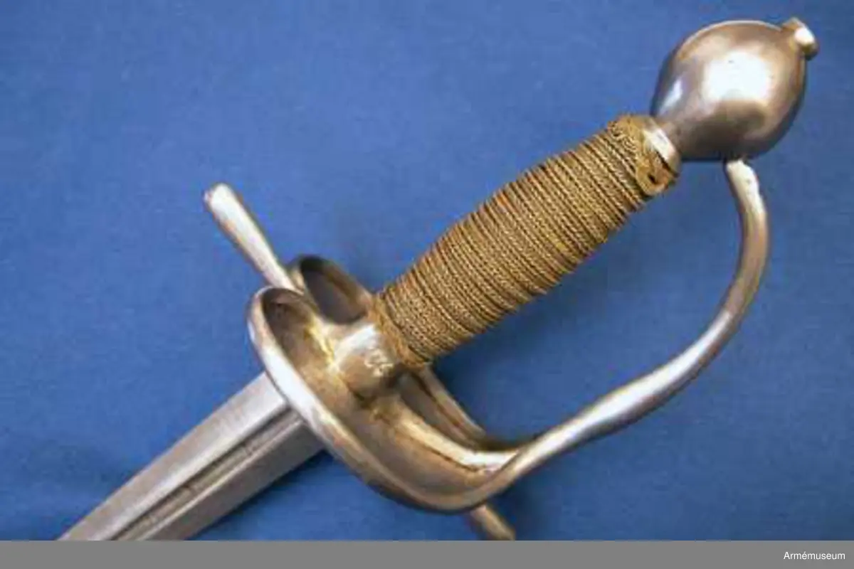 Klingan är tveeggad med flata åsar. Upptill på var sida har den en blodrand, som på yttersidan är 16,5 cm lång. Under den nedra ändan på varje blodrand finnes ett av prickar bestående onament.

Fästet är av polerat järn och av drabanttyp. Knappen är svagt ellipsiodisk med rygg fram och bak. Diam. sidled är 3,95 cm, men över ryggarna 4,15 cm. Höjden är 4,3 cm. Nitknappen är låg och närmast cylindrisk. Halsen är ävenledes låg med konisk. Höjden av hals, knapp och nitknapp är sammanlagt 5,25 cm. 
Kaveln är spolformig med flat rand fram och bak, men sidorna är avrundade. Upp- och nedtill omgives den av en ringliknande, platt flätning, "krans", av rätt varierande bredd, i huvudsaken dock 0,7 cm, vilken flätning består av mässingstråd, men är hopsnodd av två parter. I övrigt är kaveln lindad med 4 mässingstrådar, av vilka två är rätt grova, den ena höger- den andra vänstersnodd, men de båda övriga rätt fina.
Parerstången är nästan rak och blir mot ändarna litet bredare. Den främre änden är avrundad, men den bakre har mer tvär avslutning. Armarna ha spetsovalt tvärsnitt. Den största bredden är för den främre armen 1,1 cm, men för den bakre 1,25 cm. Den största tjockleken är för bägge armarna 0,85 cm. Avståndet mellan den främre eggen och parerstångens främre ändan är 6,8 cm, men mellan den bakre eggen och den bakre änden 5,9 cm. 
Parerplåten är hjärtformig och har förhöjda kanter, vilka sistnämda egentligen bestå av spänger, en på var sida, vilka från parerstångens bakre arm gå till handbygelns nedre del. Tomrummen mellan spängerna och parerstången, resp. handbygelns nedre del, ha utfyllts med ett par kupiga plåtar, som faslötts med mässing. Parerplåten är något större på ytter- än på insidan. Avståndet mellan klingans mitt och parerplåtens kant är på det förstnämda stället 4,6 cm, men på det sistnämda 4,5 cm. 
Handbygeln utgår från korset, har spetsovalt tvärsnitt och den största bredden litet ovanför parerplåtens spets. Dess övre ända är instucken i ett hål i knappen. På handbygelns innersida nära övre ändan är bokstäverna AD inslagna. Tumbygel finnes icke.