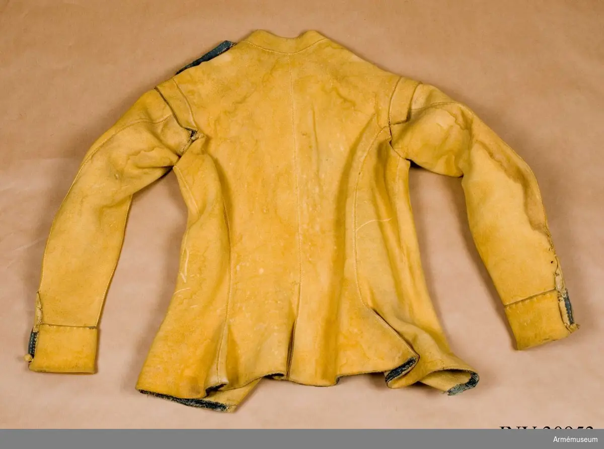 Kyller av gul älghud med smala blå linneband som kantning på insidan samt som passpoal vid övre kant av ärmuppslagen.
Helt framstycke med utsvängt kort skört med uppvik framtill, samt bakstycke med mitt-bak-söm och två sidstycken. Sidsöm under ärmen. Formad tvåsömsärm med ärmuppslag. Ärmuppslagen har sprund som knäpps med 3 koniska älghudsknappar i varje sida, även om det är utskuret 6 knapphål i höger ärm och 5 i den vänstra. De knapphål som inte används är ihopsydda. Liten axelkarm, samt axelklaffar på båda sidor som är fastsydda vid axelsömmen samt knäpps med älghudsknapp vid halsen. Knapp saknas på vänster axel.
Låg ståndkrage som har varit kantad på insidan med blått band. Detta saknas i dag.
Plagget knäpps kant i kant med 12 stycken hyskor och hakar mitt fram. Alla sömmar är sydda med oblekt lintråd.
Märkt inuti ryggen "No 1".
Kyllret skiljer sig något från samtida kyller av samma modell genom att de blå banden är smalare.