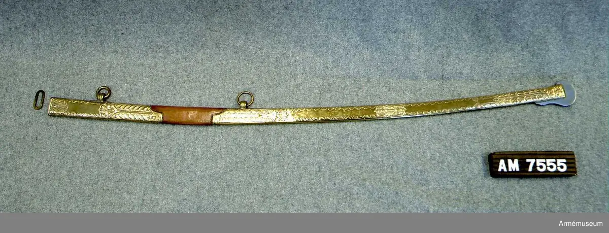 Balja med beslag av förgylld mässing, mittparti läderklätt. Släpsko av stål. Baljan är av brunt läder och har munbleck och mycket lång släpsko av förgylld mässing, som är driven i stiliserade blomornament m.m. 
Släpskon är längst ned på änden och vid framsidan skodd med stål. 
Munbleckets nedre och släpskons övre kant är enkelt fasonerad. 
På ryggsidan har munblecket och släpskon var sin ögla för en koppelring. 
Dessa öglor har längs kanterna förhöjda ränder och pryds på mitten av fina prickar. 
Koppelringen är av mässing.