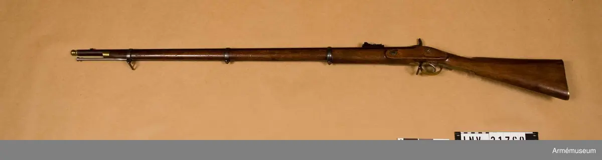 Grupp E II.
Gevär med slaglås.
Antal räfflor: 3. Räffelstigning: ett halvt varv på piplängden. Kulvikt: 34 g. Krutladdningens vikt: 4 g. Pipan är brungjord och rund, men har baktill på översidan en 3,5 cm lång avplattning. Snäckan är rätt liten. En fyrkantig kombinerad bajonett- och kornklack sitter 3,3 cm bakom mynningen och på översidan av denna klack sitter det orörliga kornet. Ramtrappsiktets fot sitter 8,9 cm framför pipans bakre ände. Siktet har gradering för avstånd mellan 100 och 900 yards= resp 90 och 810 m. På pipans översida står PRITCHETT 7 POULTRY LONDON och på vänstra sidan är två Londonstämlar inslagna.

På det gråhärdade, framåtliggande kedjelåset är hanen och låsblecket längs kanterna prydda med ett par ingraverade ränder. stocken är av valnöt. Framstocken har en avsats för vart och ett av de tre banden. Piprännan är utvidgad alldeles bakom näsblecket. Bakplåten och varbygeln är av mässing. Den förstnämnde har en ganska lång, smal flik, som går in över kolvryggen och som längst fram är fäst med en skruv, under det att två skruvar sitter i bakplåten. Geväret har egentligen ej sidbleck, utan kring vart och ett av de bägge hålen för låsskruvarna finns en smal, ringliknande mässingsskoning, från vilken en kort arm går framåt och en annan bakåt. De tre banden är av gråhärdat järn och ha på undersidan öron, som förenas genom en skruv. Det främsta bandet ligger 8 cm bakom stockens framände och skruven på detta band fasthåller den främre rembygeln. Näsblecket är av mässing, och fasthålles av en underifrån kommande skruv. Den bakre rembygeln är fäst i varbygelns främre del.

Laddstocken är av stål och har skålformigt huvud. Omkring 12 cm från framänden har laddstocken en ungefär 2,5 cm lång förtjockning, som passar i laddstocksrännans ovan omtalade utvidgning. I smaländen är laddstocken gängad på en längd av 0,8 cm. Litet bakom huvudet finns fyra nästan utslipade bokstäver (R & K?).

Om den till detta gevär använda ammunitionen, se AM 6117-6120. Uppgiften om reffelstigningen har hämtats ur Jochnick, Handgevärslära, Stockholm 1863 paragraf 60. Geväret kallas vanligen Enfield- pritchetgeväret, då det konstruerades av gevärsfabrikanten Pritchett och antogs av den i Enfield församlade gevärskommiten. Av allt att döma har alltså den ovan beskrivna gevär tillverkats av konstruktören.