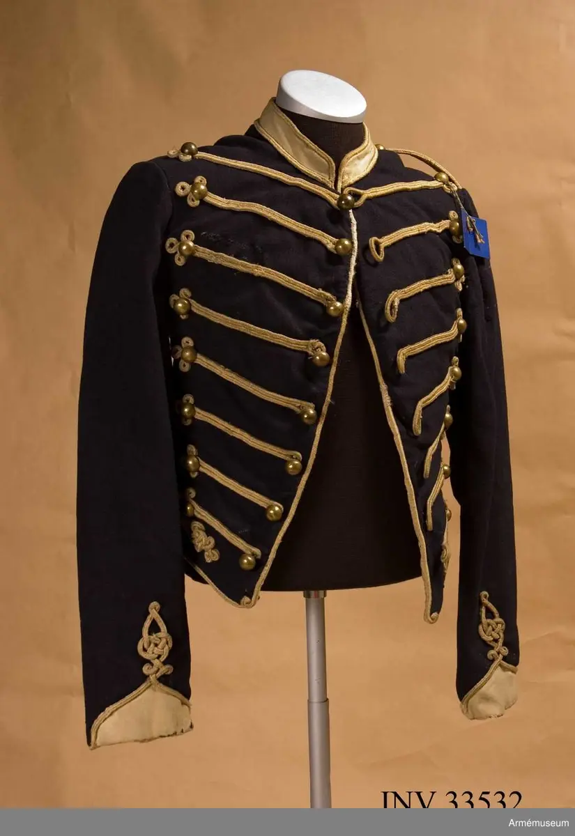 Blå dolma m/1846 med platta vita snören m/1851.

Dolman är sydd av mörkblått kommisskläde, med liten ståndkrage och ärmuppslag av vitt kläde. Helfodrad med vitt bomullstyg.
Plagget är kroppsnära, och är konstruerat med fram- och sidstycken i ett, sidstycken bak, samt helt bakstycke som går ner i en avkapad spets mitt bak. Det har midjesöm och litet skört som fortsätter bak och bildar veck vid sidsömmen. Ärmarna är ensömsärmar eller S-ärmar med fasta vita ärmuppslag som slutar i en spets upptill, och har ärmsprund som knäpps med hysk och hake.
Tvärs över bröstet löper 8 rader med snörmakerier med 3 lodräta knapprader med 8 knappar i varje. De yttre raderna har kullriga nappar medan mittenraden har klotknappar. Samtliga knappar är av mässing. Snörmakerierna är gjorda av vita fyrkantsnören, så kallade platta snören, av ull.
Plagget bär spår av att vara omsytt; bland annat är ärmarna förlängda nertill och en lång kil är iskarvad från ärmhålet till underärmen på båda ärmar. Framtill syns iskarvade kilar nertill. Det är även hårt slitet, och har flera lagade revor som uppstått under dess användningstid samt ett lappat hål på vänster ärmkulle framtill.
Innerficka i vänster framstycke, samt bröstfickor på båda sidor på utsidan, dolda under snörmakerierna.
Plagget är märkt för hand med skrivstil i ryggens fodersida, med bokstäverna W:N:S No 73, vilket troligen står för Westra Närkes Skvadron, soldatnummer 73.
På baksidan pryds dolman av snören längs med sidsömmarna som slutar i en knut upptill, samt med snörmakerier på skörtet, bland annat i form av en spiral. Även dolmans nederkant, framkant och ärmarnas nederkant pryds av snören.