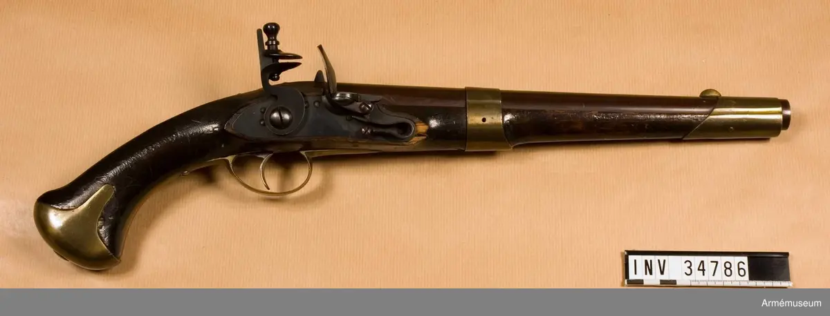 Pistol med flintlås.
Pipan är brungjord. Låset är blånerat. Pistolen har mässingsbeslag utom ryggbeslaget på kolven, vilket är av järn. På pipans kammarstycke finns en stämpel "Helvig inv.t" Kolven är märkt "I S", på vänster sida ovanför sidblecket.